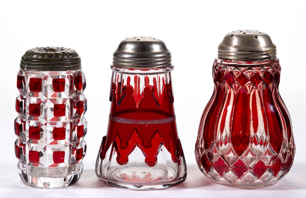 ASSORTED EAPG - RUBY-STAINED SUGAR SHAKERS, LOT OF: ASSORTED EAPG - RUBY-STAINED SUGAR SHAKERS, LOT OF THREE, colorless, comprising a McKee Gothic, a Duncan Block, and a Pioneer's Beauty, each with a period lid. Various makers. Fourth quarter 19th/firs