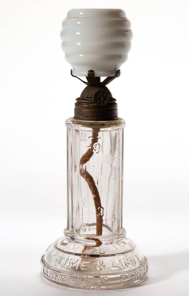 GRAND VAL'S TIME INDICATING MINIATURE LAMP: GRAND VAL'S TIME INDICATING MINIATURE LAMP, colorless, ribbed cylinder-form font with one wide panel embossed with numerals representing nighttime hours of 8 thru 12 and 1 thru 6, circular foot emboss