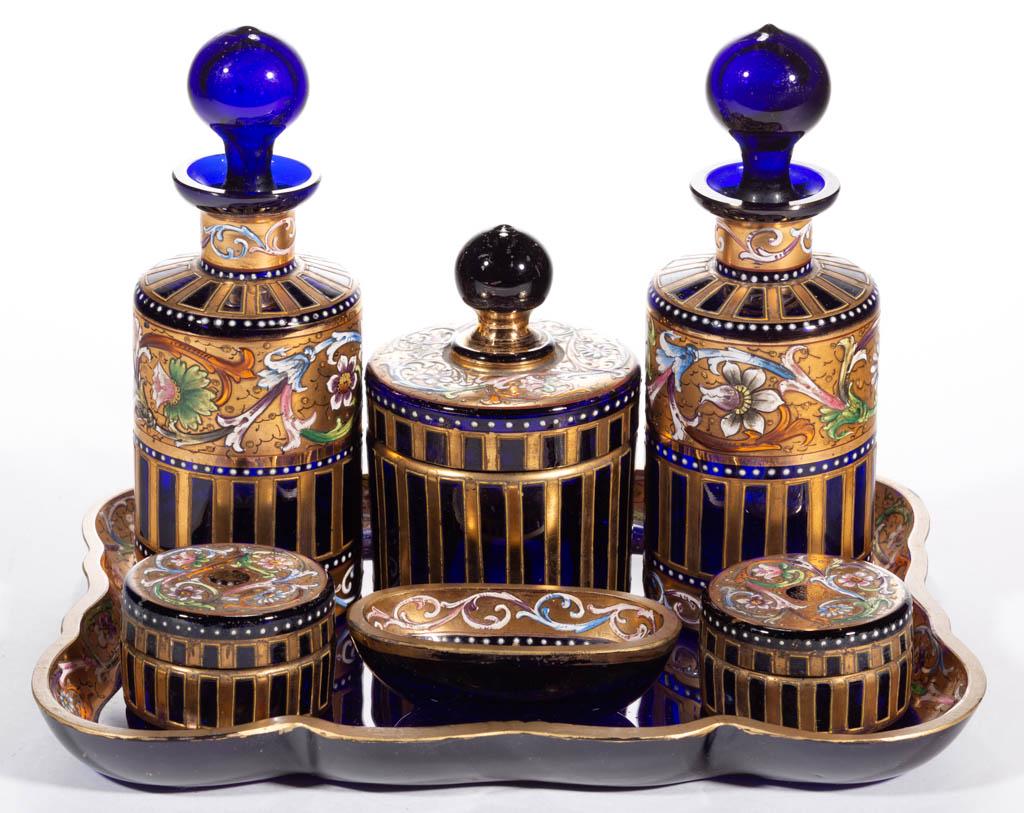 BOHEMIAN ENAMEL-DECORATED GLASS SEVEN-PIECE DRESSER SET: BOHEMIAN ENAMEL-DECORATED GLASS SEVEN-PIECE DRESSER SET, cobalt blue with matching polychrome-enamel decoration, comprising two perfume bottles, a puff jar, two salve jars, a brush holder, and an unde