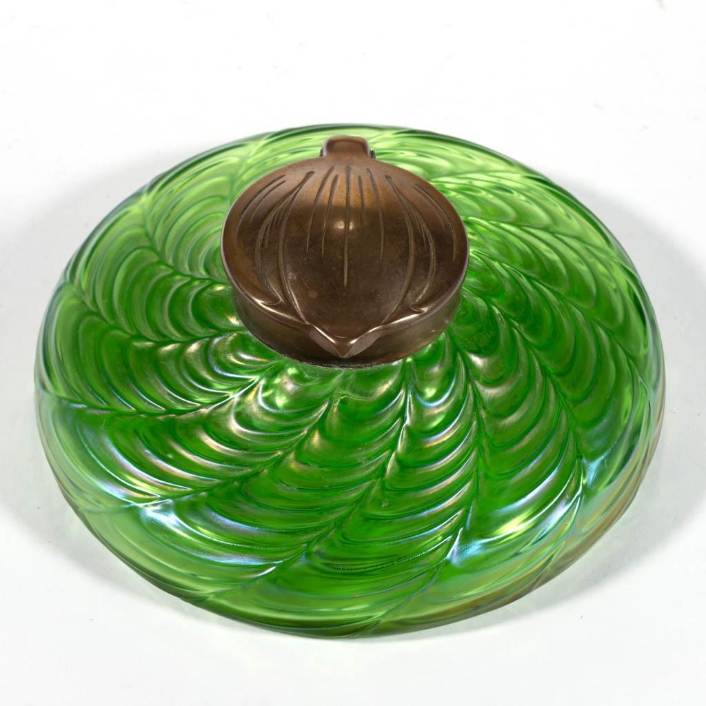 LOETZ-TYPE BOHEMIAN ART GLASS INKWELL: LOETZ-TYPE BOHEMIAN ART GLASS INKWELL, green iridescent, low circular form with swirled feather design, hinged brass cover and glass insert. First quarter 20th century. 1 3/4" H, 5 1/4" D.Glass insert