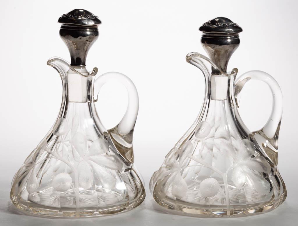 AMERICAN INTAGLIO CUT GLASS PAIR OF DECANTERS: AMERICAN INTAGLIO CUT GLASS PAIR OF DECANTERS, colorless, each tapered form with cut panels to the body, floral decoration, applied handles, fitted with original stoppers having sterling silver-mounte