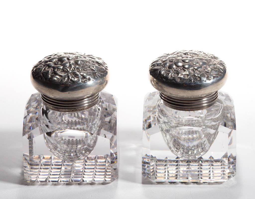 AMERICAN CUT GLASS INKWELLS, LOT OF TWO: AMERICAN CUT GLASS INKWELLS, LOT OF TWO, colorless, each square form with a cut-faceted shoulder and cross-hatched box bases, each with sterling silver mounts and floral repousse lids. Silver lids wit