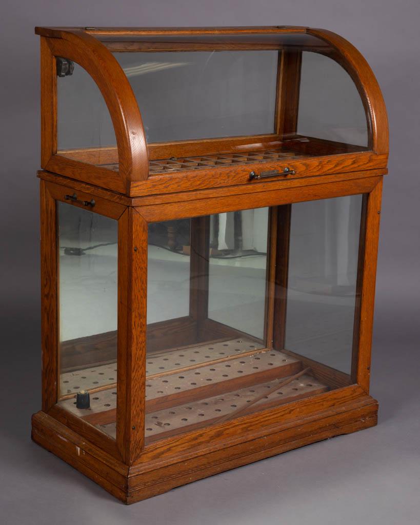 OAK COUNTRY STORE CANE / UMBRELLA SHOWCASE: OAK COUNTRY STORE CANE / UMBRELLA SHOWCASE, with slanted hinged lift top, and fitted interior, the whole raised on casters, retains plaque for "MOXEY, GILL & HOWLETT / MAKERS / PHILADELPHIA, PA". Reta