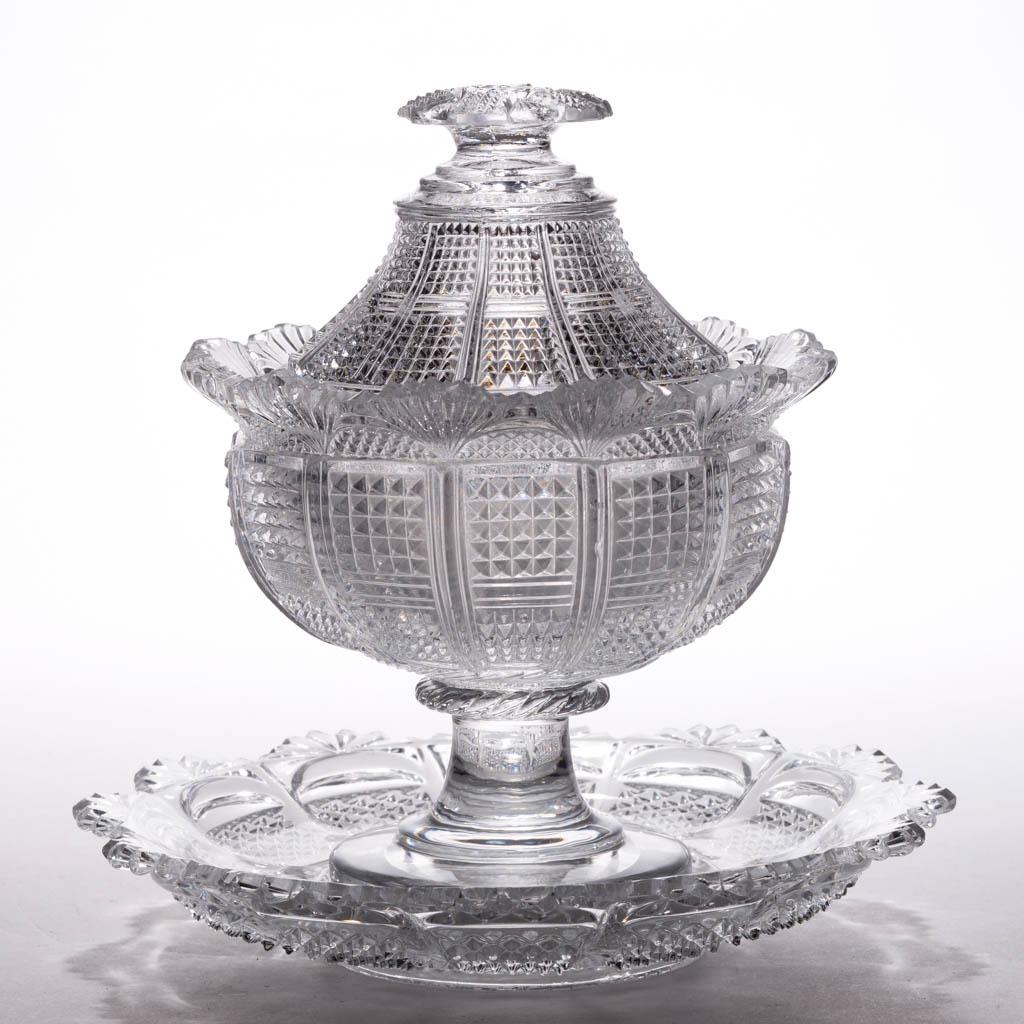 FRENCH PRESSED GLASS COVERED COMPOTE AND UNDERPLATE: FRENCH PRESSED GLASS COVERED COMPOTE AND UNDERPLATE, colorless lead glass, 12-panel pattern with bisected squares of pyramids, overhanging fan rim and six-point star finial, raised on a flaring stem a