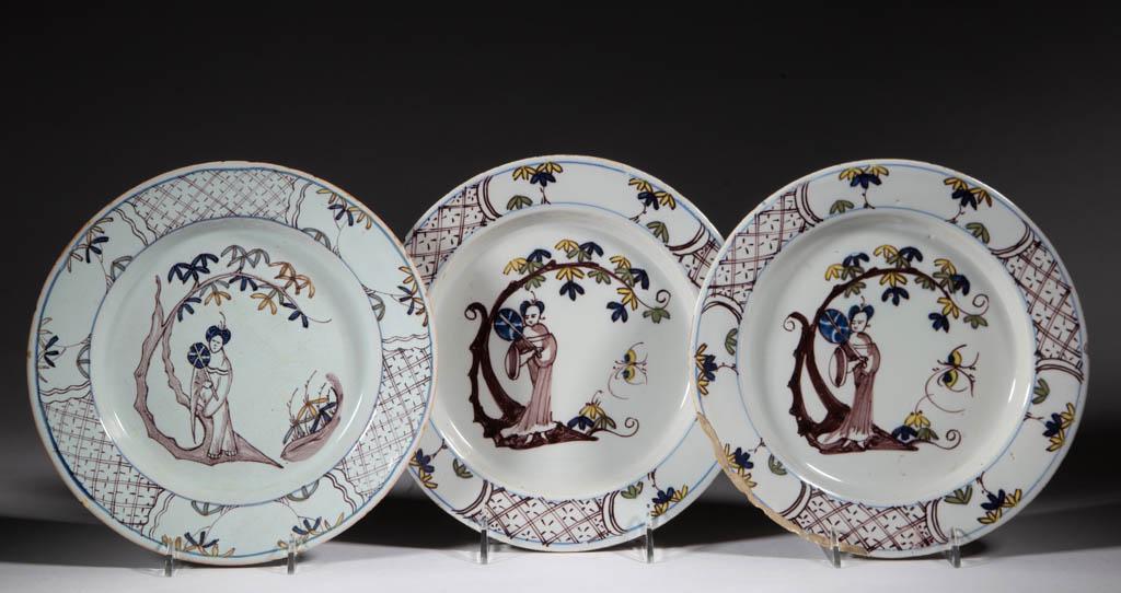 ENGLISH DELFT TIN-GLAZED CHINOISERIE EARTHENWARE: ENGLISH DELFT TIN-GLAZED CHINOISERIE EARTHENWARE PLATES, LOT OF THREE, each having central polychrome hand-painted image of a woman standing beneath a tree holding a parasol, having alternating panell
