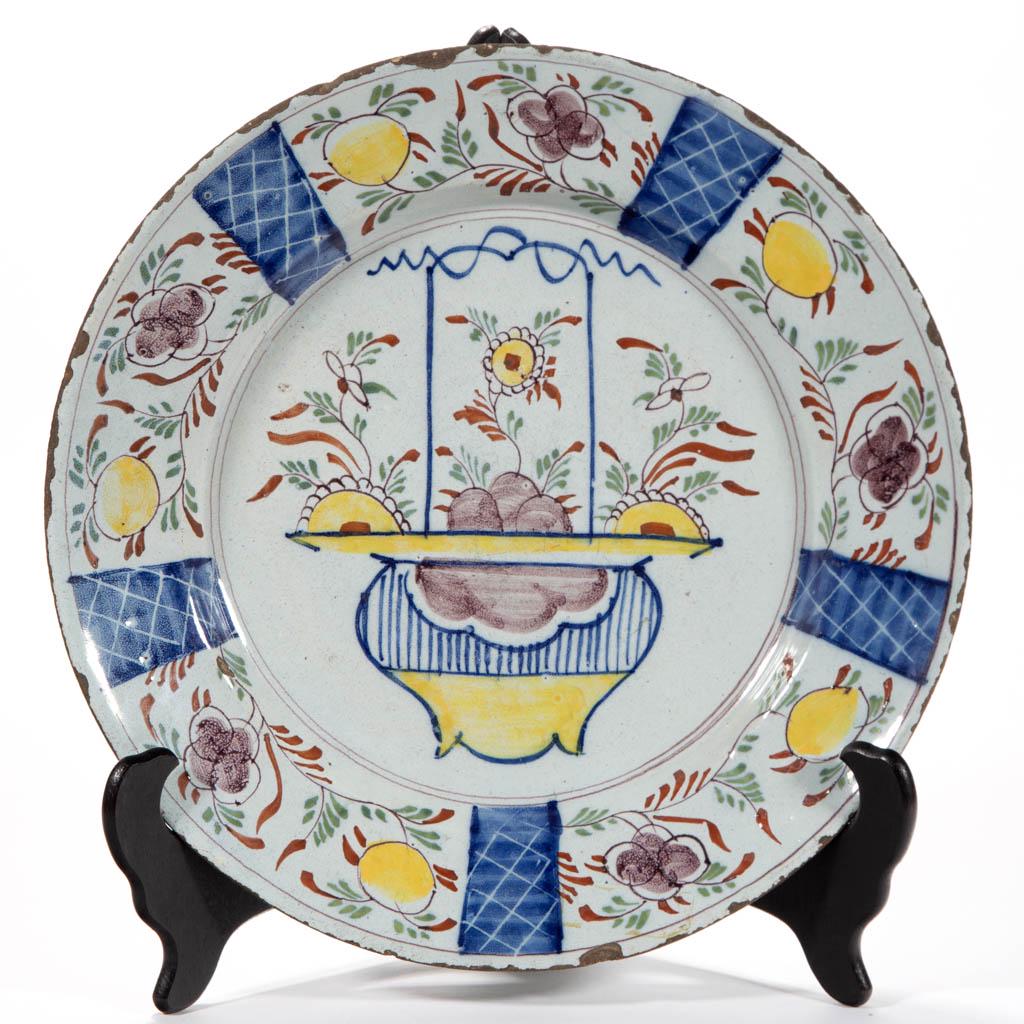 ENGLISH DELFT TIN-GLAZED EARTHENWARE CHARGER: ENGLISH DELFT TIN-GLAZED EARTHENWARE CHARGER, having bright polychrome hand-painted decoration featuring a flower-filled basket in center, with single pierced hole to foot ring for hanging. Having ent