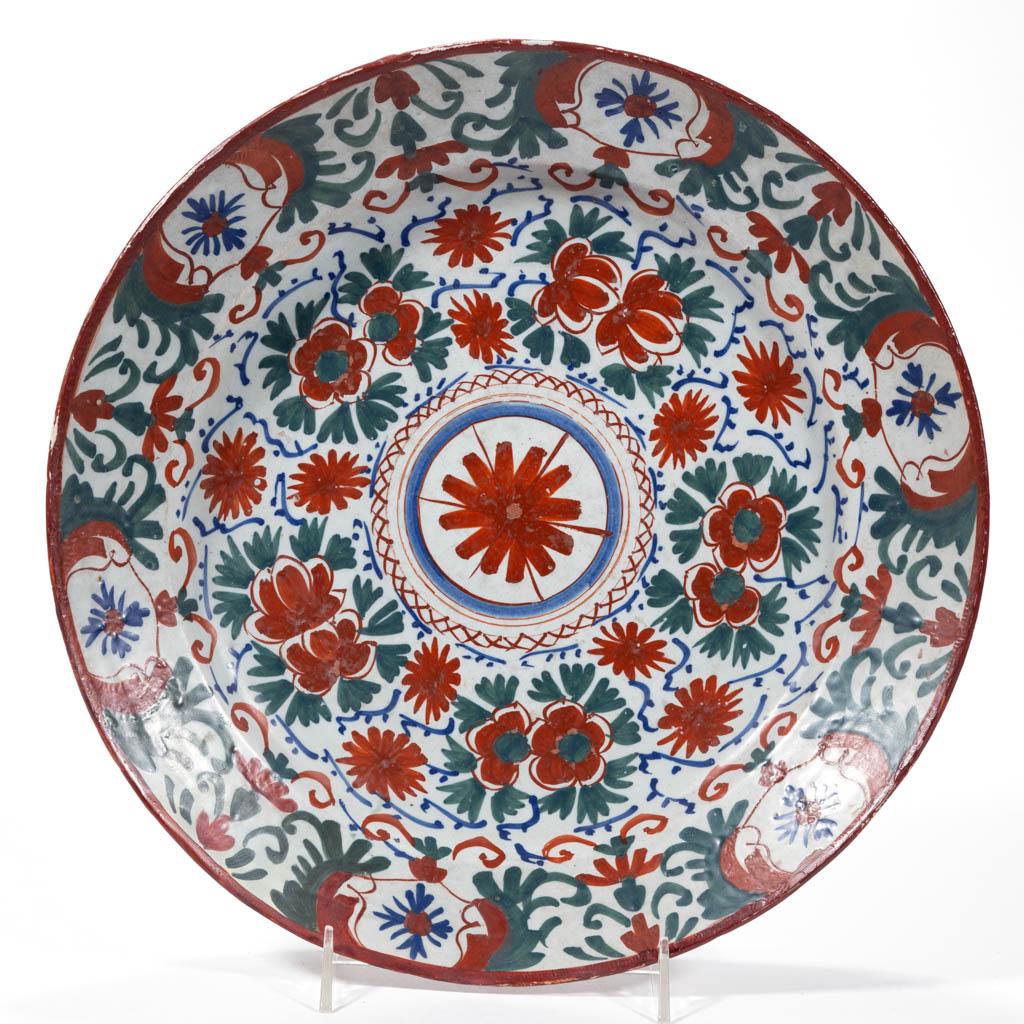 ENGLISH DELFT TIN-GLAZED EARTHENWARE CHARGER: ENGLISH DELFT TIN-GLAZED EARTHENWARE CHARGER, having bold polychrome floral decoration with a central stylized flower, having drilled hole to foot ring for hanging. Unmarked. 18th century. 13 1/2" D. 