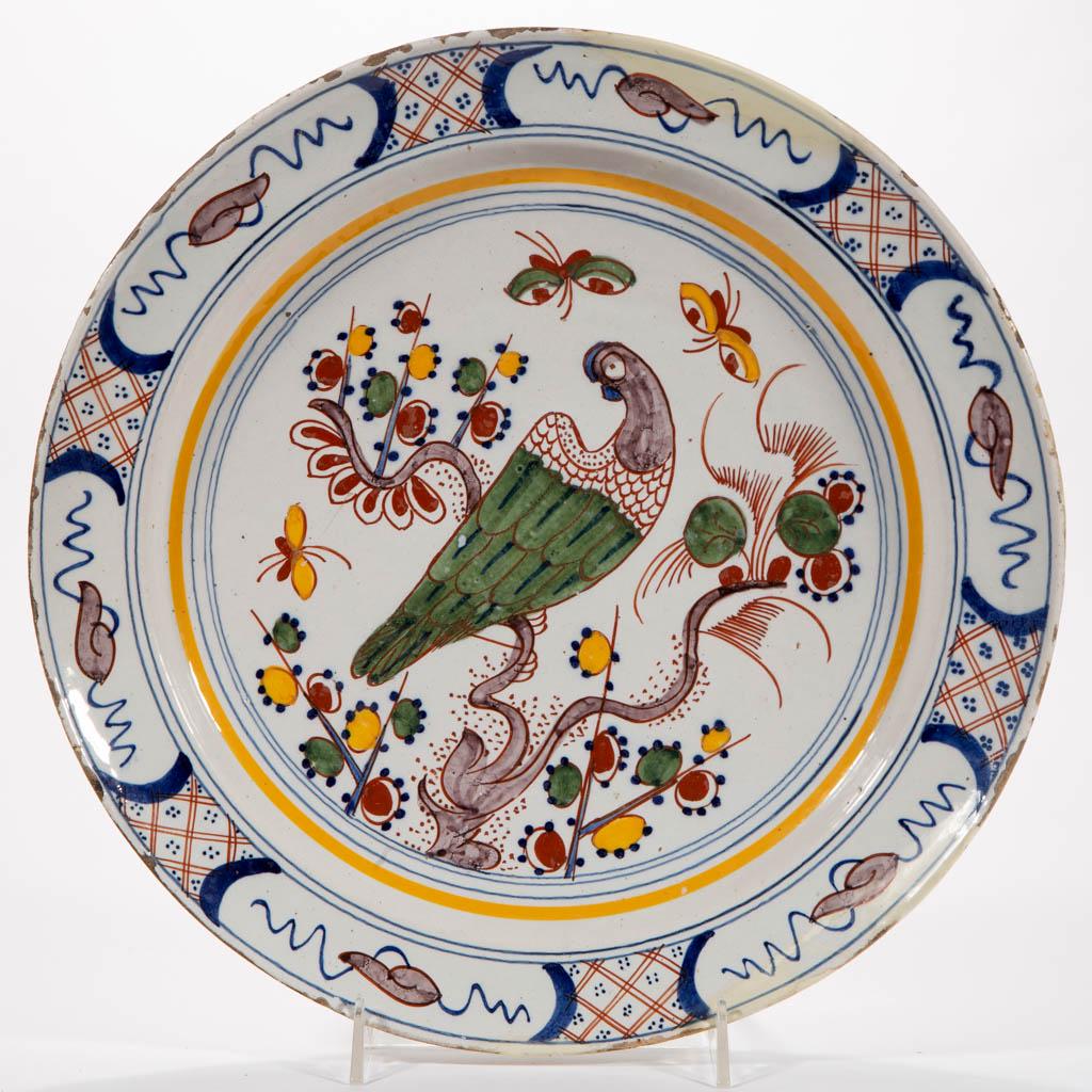 ENGLISH DELFT TIN-GLAZED EARTHENWARE CHARGER: ENGLISH DELFT TIN-GLAZED EARTHENWARE CHARGER, featuring a bright polychrome bird perched on a stylized tree with three butterflies, having single pierced hole to foot ring for hanging. Unmarked. Secon