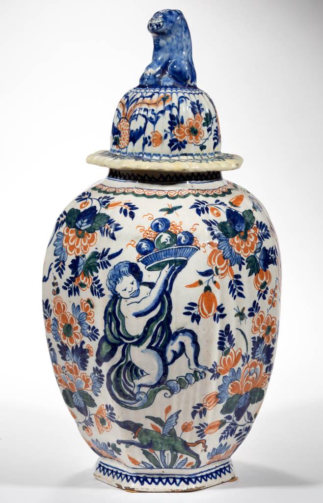 DUTCH DELFT TIN-GLAZED EARTHENWARE JAR AND COVER: DUTCH DELFT TIN-GLAZED EARTHENWARE JAR AND COVER, baluster form, featuring two children, to opposite sides, wearing flowing material and lifting trays of fruit with leaping dogs below, and two peacock