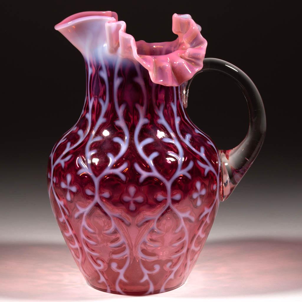 OPALINE BROCADE / SPANISH LACE WATER PITCHER: OPALINE BROCADE / SPANISH LACE WATER PITCHER, cranberry opalescent, shouldered form with three-section crimped and ruffled rim, applied colorless handle. Northwood Glass Co. Pattern introduced 1899. 9