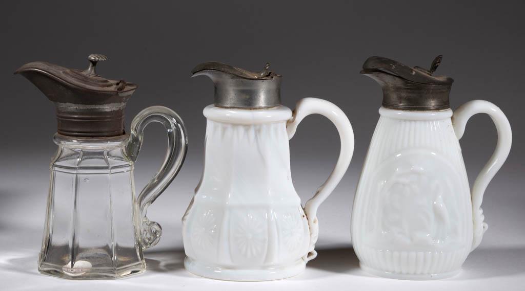 ASSORTED BLOWN-MOLDED SYRUP PITCHERS, LOT OF THREE: ASSORTED BLOWN-MOLDED SYRUP PITCHERS, LOT OF THREE, colorless and opaque white, comprising an octagonal, a Beehive, and an Eight-Panel Rosette, each having a period lid. Various makers. 19th century. 