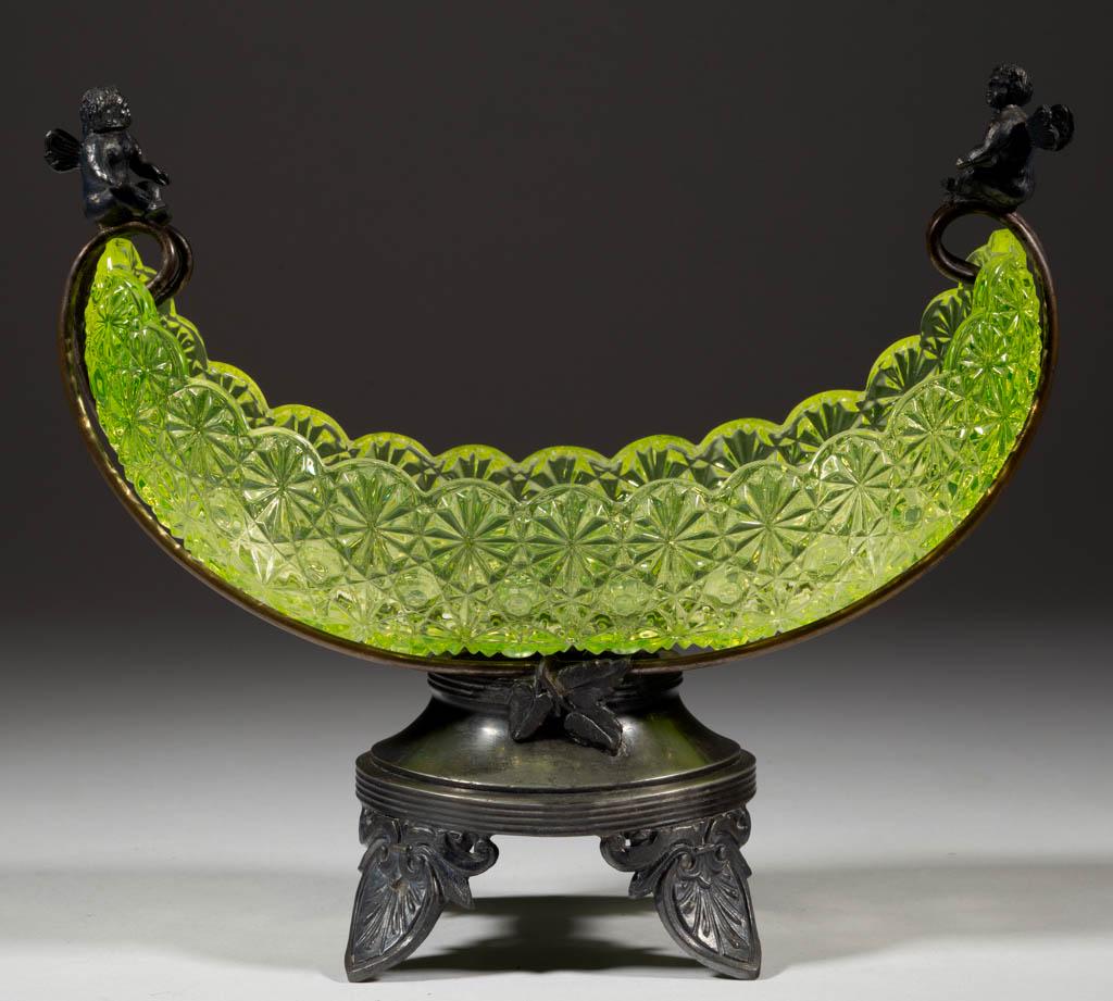 DAISY AND BUTTON VASELINE CANOE DISH WITH STAND: DAISY AND BUTTON VASELINE CANOE DISH WITH STAND, Vaseline (reacts under black light), metal stand having two cherubs sitting on top of the handles and base raised on four anthemion leaf-shaped feet, m