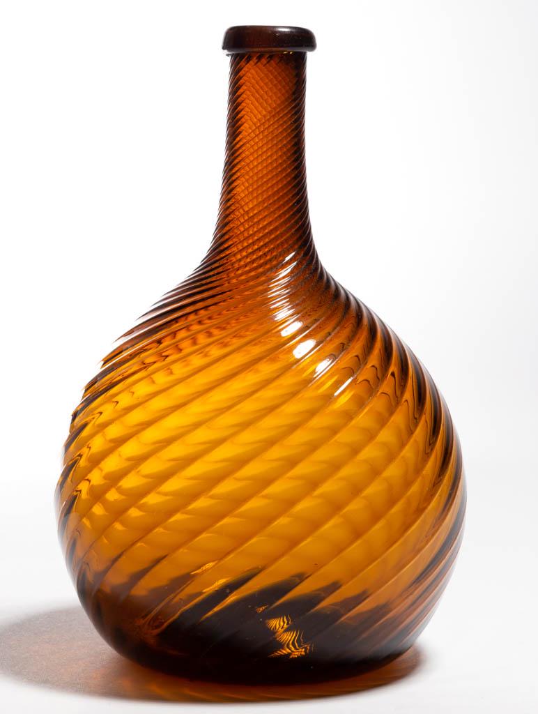 PATTERN-MOLDED GLOBULAR-FORM BOTTLE: PATTERN-MOLDED GLOBULAR-FORM BOTTLE, golden amber, 24 ribs swirled to the right, medium neck tapering slightly to a turned-over mouth, rough pontil mark. Midwestern, possibly White Glass Works, Zanesv