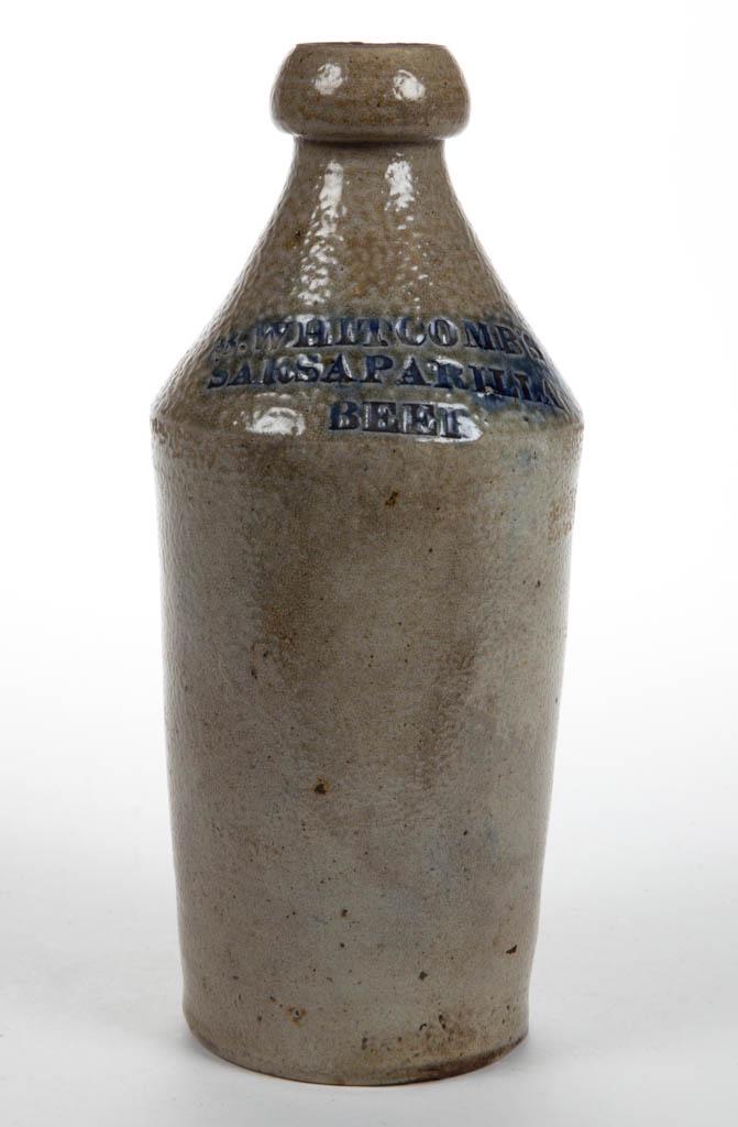 WHITCOMB STONEWARE SARSAPARILLA BEER BOTTLE: WHITCOMB STONEWARE SARSAPARILLA BEER BOTTLE, salt-glazed, cylindrical form with sharp shoulder, stamped "B. WHITCOMB'S / SARSAPARILLA / BEER" on shoulder, brushed cobalt highlighting stamp, broad roun