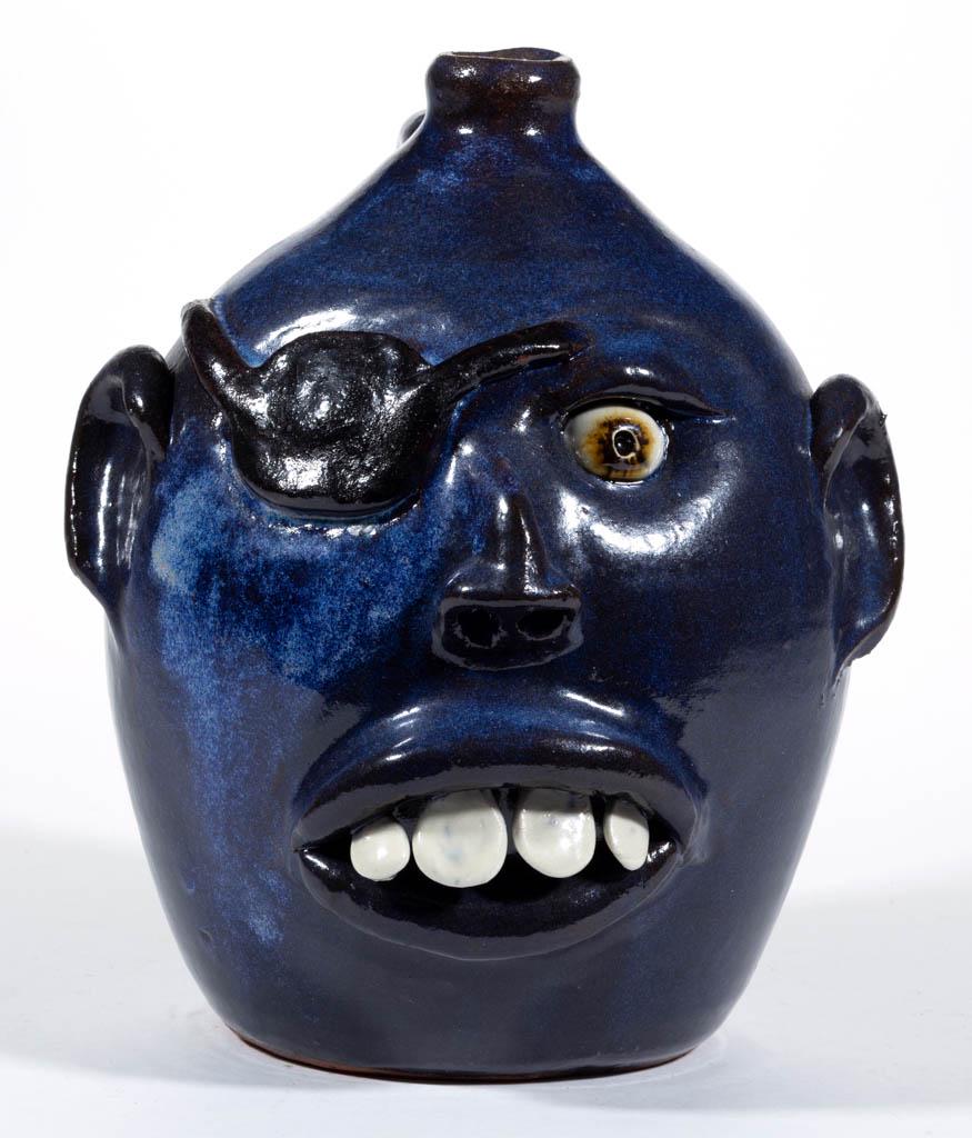 SIGNED BILLY JOE CRAVEN (B. 1947), GEORGIA STONEWARE: SIGNED BILLY JOE CRAVEN (B. 1947), GEORGIA STONEWARE FACE JUG, having rich blue glaze with hand-modeled features including an inset ceramic eye, right eye covered by a patch, applied ears and nose, an
