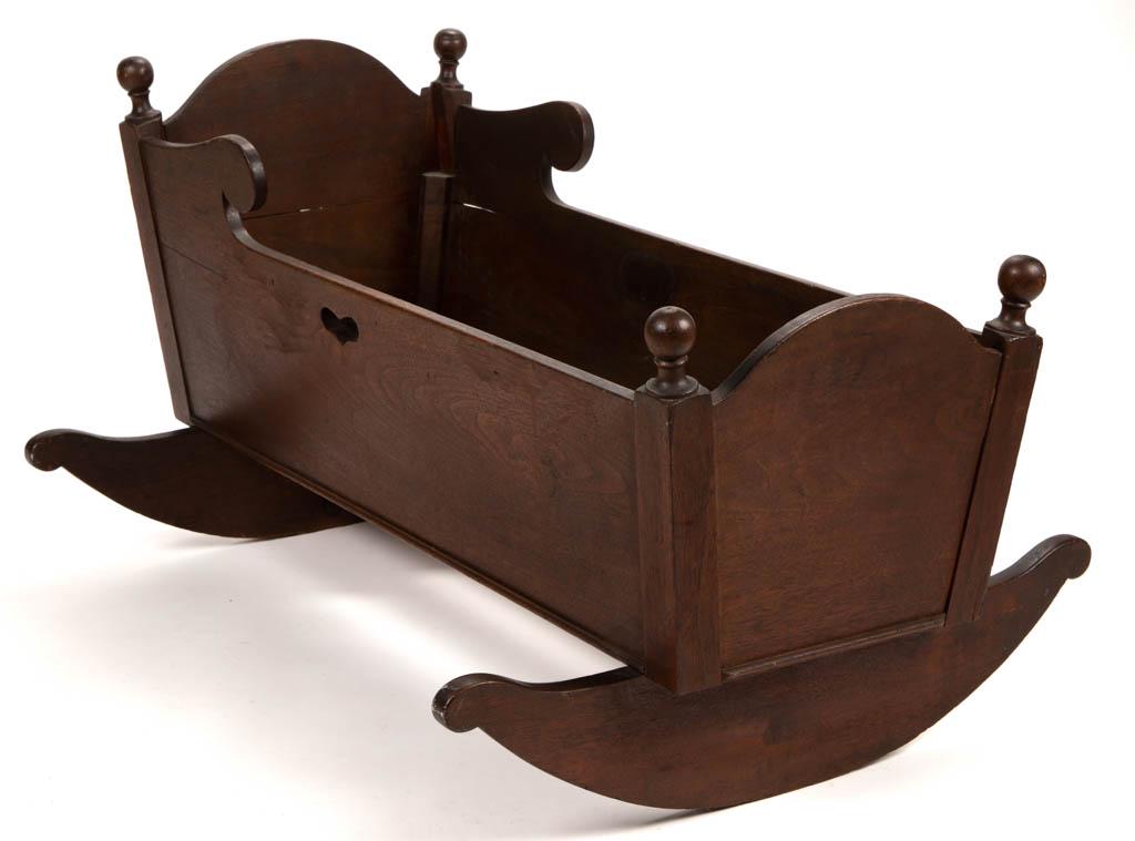 AMERICAN WALNUT CRADLE: AMERICAN WALNUT CRADLE, featuring post finials, cut-out sides and heart-shapes on the sides with applied metal on the interior, raised on "cheese-cutter" rockers. Retains likely original varnished sur