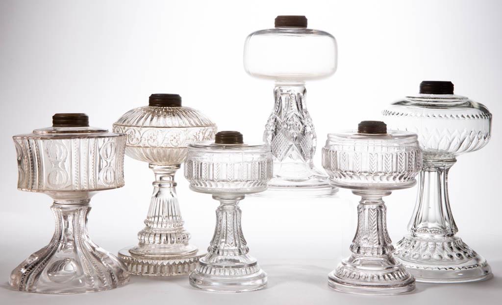 ASSORTED GLASS KEROSENE STAND LAMPS, LOT OF SIX: ASSORTED GLASS KEROSENE STAND LAMPS, LOT OF SIX, colorless, including a Grace, a Dogtooth, and a Famous example. Various makers. Late 19th/first quarter 20th century. 7 5/8" to 10" H. Grace having som