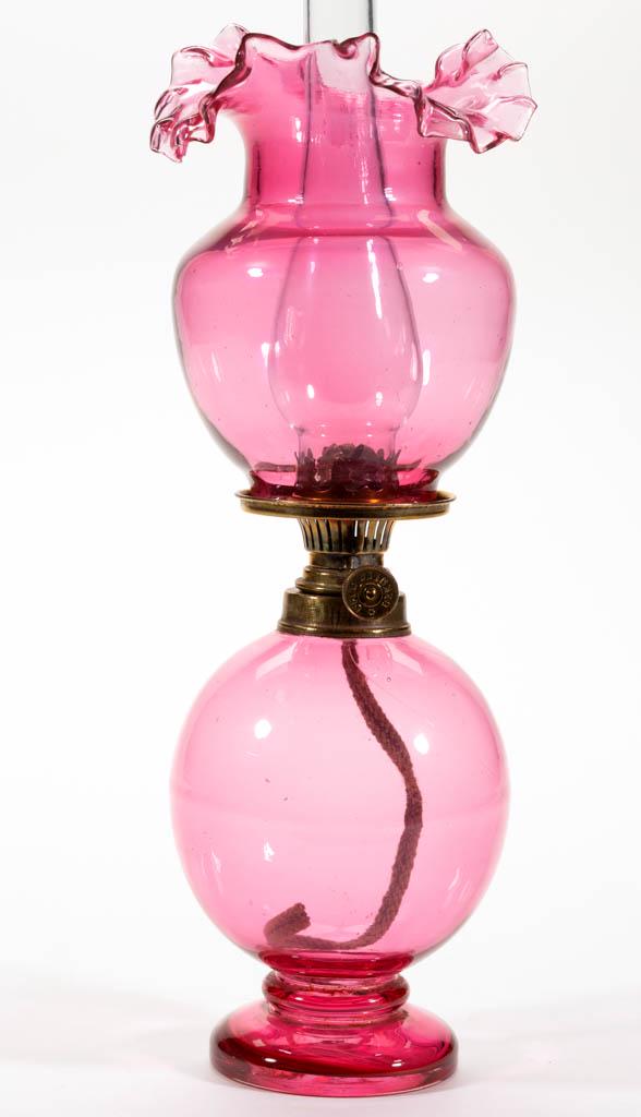 CASED GLASS MINIATURE STAND LAMP: CASED GLASS MINIATURE STAND LAMP, cased pale cranberry, elongated-form font with short pedestal foot, matching shade with folded-out and crimped rim, period collar. Fitted with a Spar Brenner burner, 