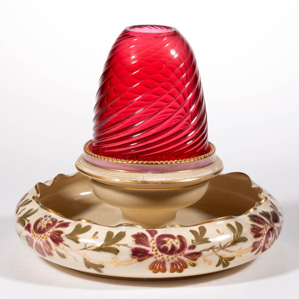 PATTERN-MOLDED SWIRLED RIB GLASS AND ENGLISH CERAMIC: PATTERN-MOLDED SWIRLED RIB GLASS AND ENGLISH CERAMIC FAIRY LAMP, cranberry/ruby, fairy-size dome fitted on a polychrome-enamel and gilt-decorated ceramic base with ruffled-rim flower trough. Edge of d