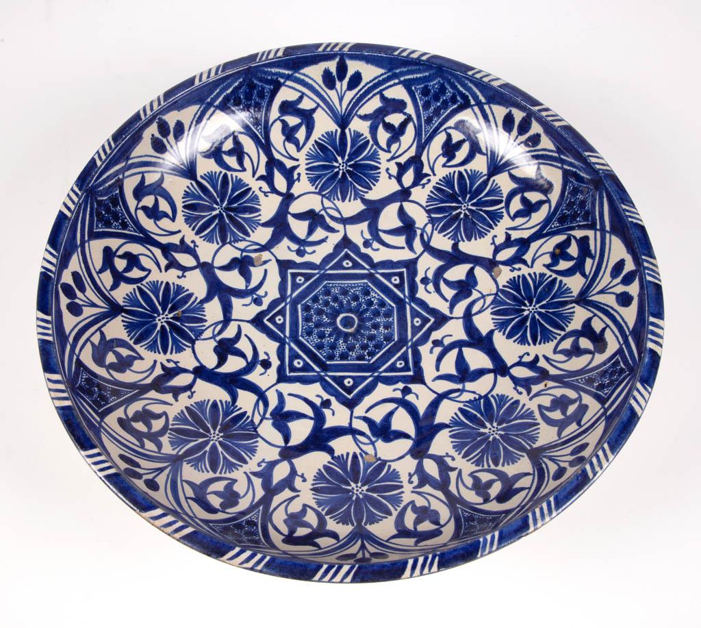 PERSIAN / ISLAMIC / IZNIK-STYLE TIN-GLAZED EARTHENWARE: PERSIAN / ISLAMIC / IZNIK-STYLE TIN-GLAZED EARTHENWARE FOOTED CHARGER, featuring deep blue floral designs with two holes to foot ring for hanging. Signed. 17th-19th century. 4" H, 15 3/4" D rim. Havin