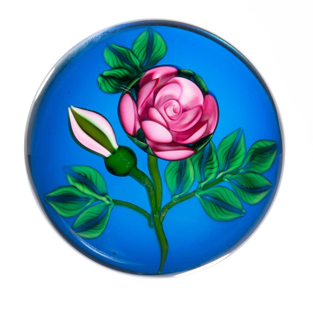 KEN ROSENFELD FLORAL LAMPWORK STUDIO ART GLASS: KEN ROSENFELD FLORAL LAMPWORK STUDIO ART GLASS PAPERWEIGHT, colorless with a blue ground, central stem supporting a pink bloom, pink and green bud to the left, 12 swirled leaves, signed to the side "K