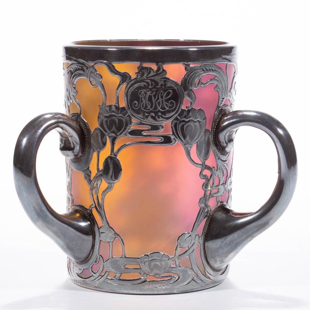 LOETZ RAINBOW IRIDESCENT ART GLASS - SILVER-OVERLAY: LOETZ RAINBOW IRIDESCENT ART GLASS - SILVER-OVERLAY LOVING CUP, three applied handles with overlay, floral motif with central monogram, polished pontil mark. Bohemia, now Czech Republic. First quarter