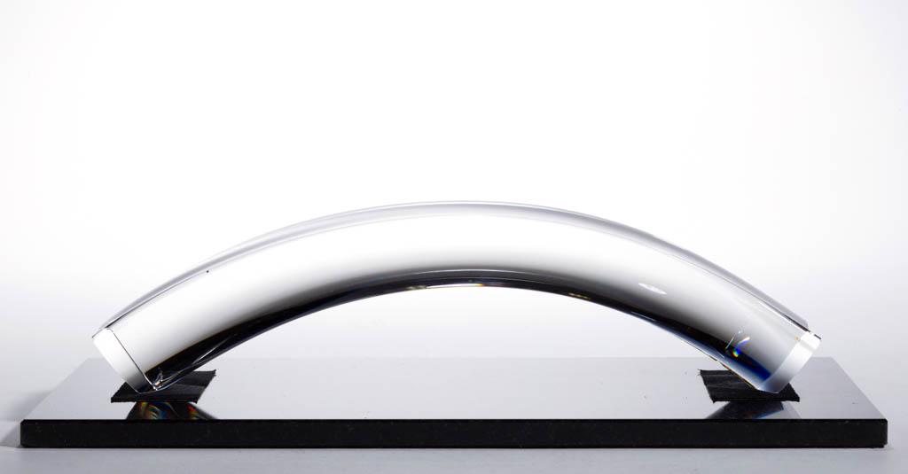 STEUBEN PARTNERSHIP ART GLASS SCULPTURE: STEUBEN PARTNERSHIP ART GLASS SCULPTURE, arching colorless sculpture with a rectangular black stone base with black pads. Steuben Glass Works; designed by Robert Cassetti. Circa 1994. 3 1/4" HOA, 10 1