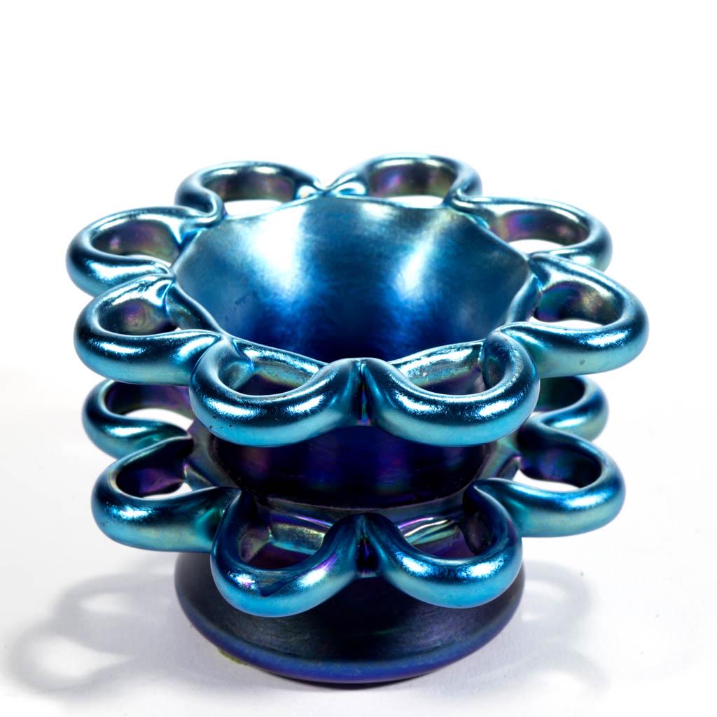 TIFFANY FAVRILE ATTRIBUTED IRIDESCENT ART GLASS FLOWER: TIFFANY FAVRILE ATTRIBUTED IRIDESCENT ART GLASS FLOWER FROG, blue iridescent, having two tiers of loopings, small hole to base, unsigned. Tiffany Studios. Early 20th century. 2 1/4" H, 3 1/2" DOA rim,