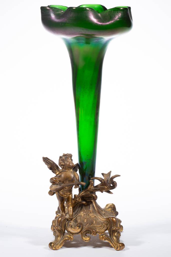 IRIDESCENT ART GLASS EPERGNE: IRIDESCENT ART GLASS EPERGNE, green iridescent, blooming flora form vase, fitted into a cast-metal square base featuring a cherub playing a mandola. Maker unverified. First half 20th century. 13 1/2" 