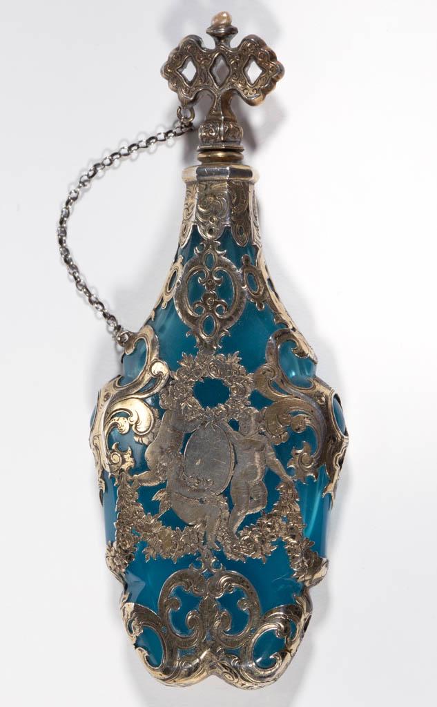 CONTINENTAL OPALINE GLASS -SILVER-PLATE OVERLAY SCENT: CONTINENTAL OPALINE GLASS -SILVER-PLATE OVERLAY SCENT BOTTLE, blue opaline, tall form with cut notches to the side, overlay depicting scrolling and cherubs, original stopper, comes with original bag m