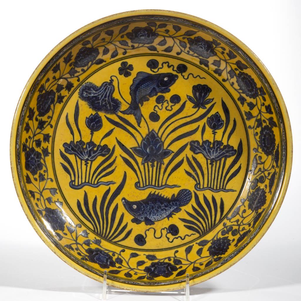 CHINESE EXPORT MING-STYLE PORCELAIN DISH: CHINESE EXPORT MING-STYLE PORCELAIN DISH, featuring underglaze dark blue hand-painted central fish and lotus/water flower design with floral border on mustard ground, having blue six character Xuande 