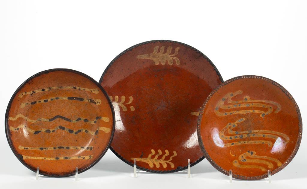 AMERICAN DECORATED EARTHENWARE / REDWARE TABLE: AMERICAN DECORATED EARTHENWARE / REDWARE TABLE ARTICLES, LOT OF THREE, lead-glazed interior, each featuring yellow slip decorations, comprising two plates having coggled rims including one featuring t