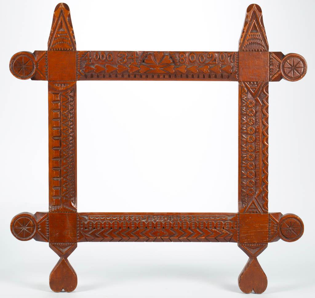 AMERICAN FOLK / TRAMP ART CARVED WOODEN FRAME: AMERICAN FOLK / TRAMP ART CARVED WOODEN FRAME, featuring serial numbers "40034 / 800207" and dated "1902", with carved hearts and hex signs. Retains original stained / varnished surface with warm colo