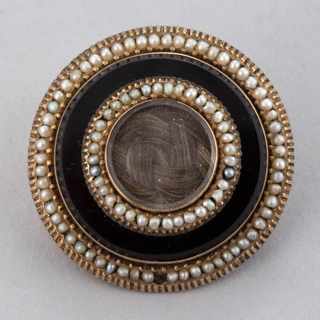 VICTORIAN HAIR-WORK MOURNING BROOCH: VICTORIAN HAIR-WORK MOURNING BROOCH, center featuring woven hair under a bevel-edged glass, surrounded by two halos of seed pearl beads and onyx-type ring, back engraved "Lou" to center having a pin f