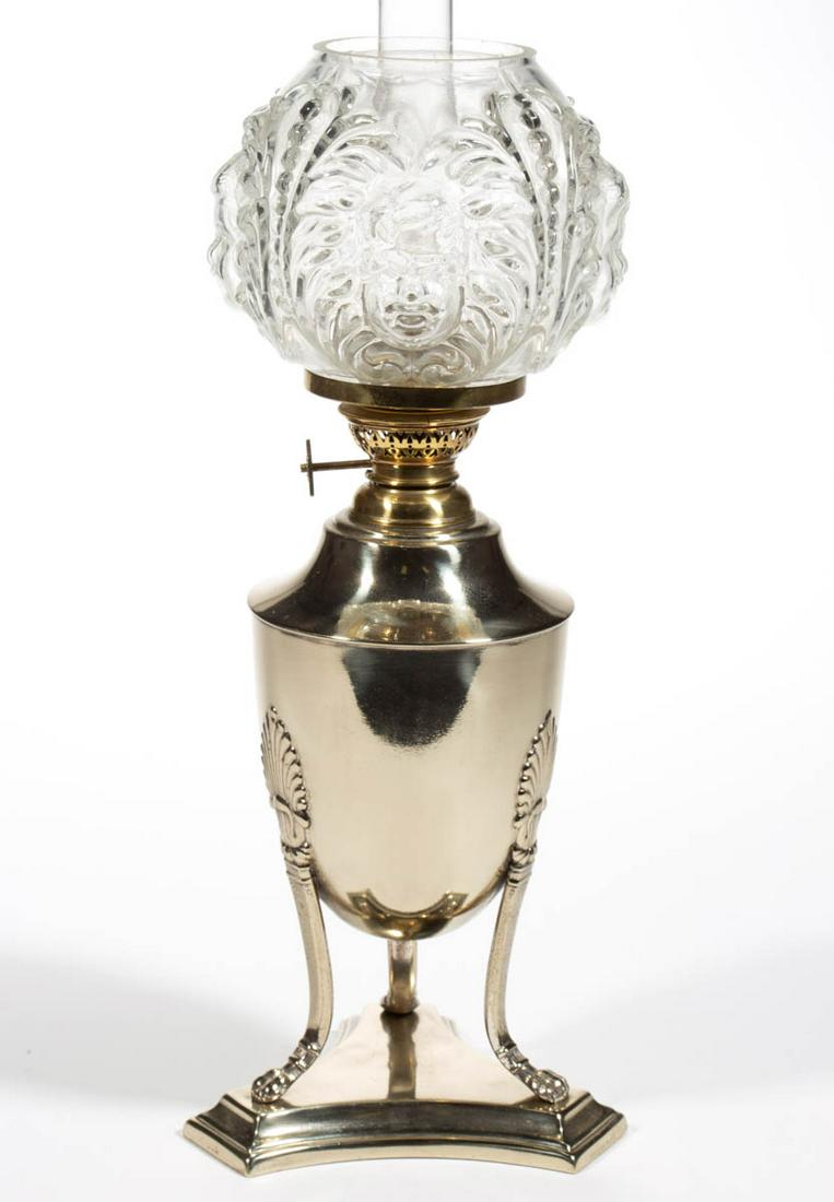 BRASS AND METAL JUNIOR LAMP: BRASS AND METAL JUNIOR LAMP, nickel-plate finish, urn-form font supported by three tapered legs with hoof tips, attached to a triangular-form stepped base, colorless non-period ball-form shade with he