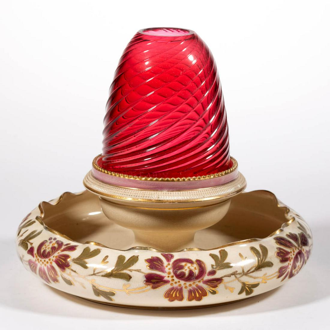 PATTERN-MOLDED SWIRLED RIB GLASS AND ENGLISH CERAMIC: PATTERN-MOLDED SWIRLED RIB GLASS AND ENGLISH CERAMIC FAIRY LAMP, cranberry/ruby, fairy-size dome fitted on a polychrome-enamel and gilt-decorated ceramic base with ruffled-rim flower trough. Edge of d