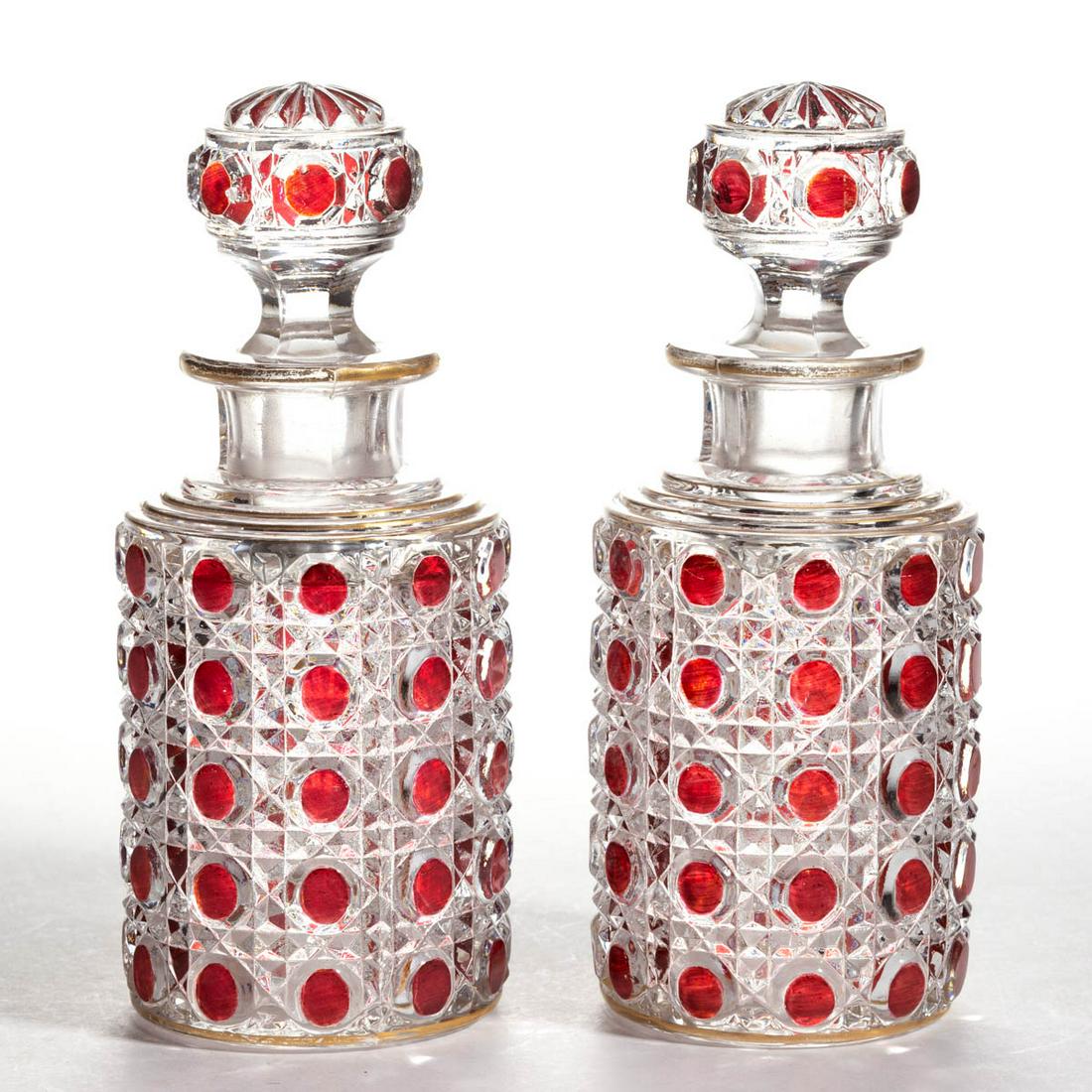 PRESSED HOB AND LACE - RUBY-STAINED PAIR OF COLOGNE: PRESSED HOB AND LACE - RUBY-STAINED PAIR OF COLOGNE BOTTLES, colorless with gilt decoration, each cylindrical-form with a four-stepped shoulder, matching pattern stopper, polished pontil mark. Maker u