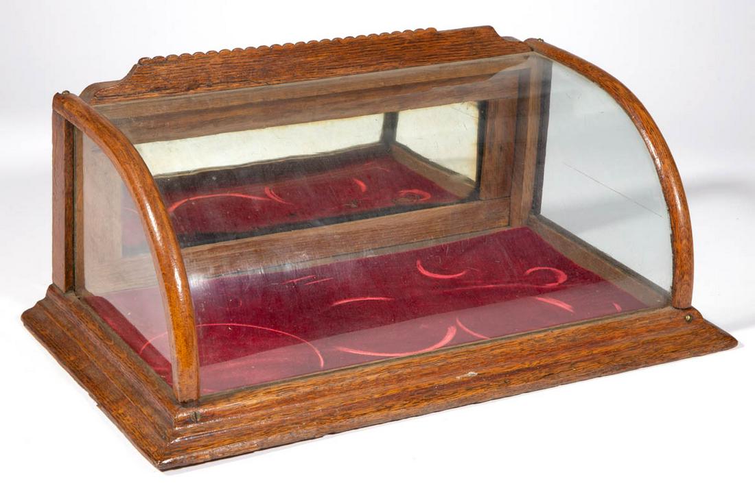 DIMINUTIVE OAK GENERAL STORE COUNT-TOP SHOWCASE: DIMINUTIVE OAK GENERAL STORE COUNT-TOP SHOWCASE, with curved-glass front panel, and applied shaped molding. Old surface with warm color. Late 19th/early 20th century. 7 1/2" HOA, 17 1/4" W, 9 1/2" D.G