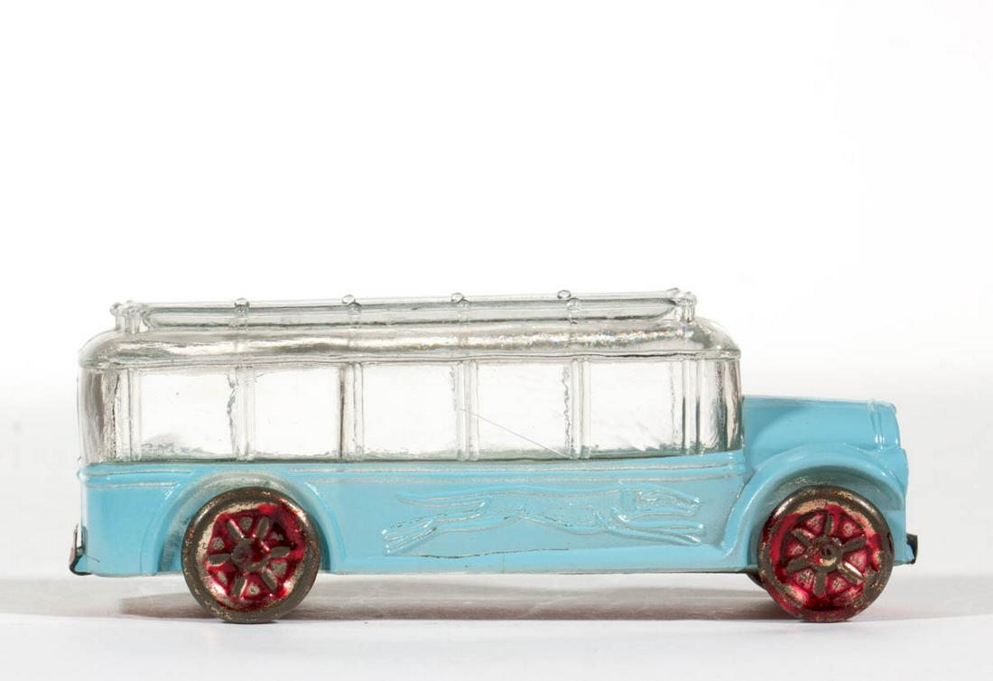 GREYHOUND BUS FIGURAL GLASS CANDY CONTAINER: GREYHOUND BUS FIGURAL GLASS CANDY CONTAINER, colorless with original paint, top embossed "V. G. CO. / JE'NE'T. / PA. / U.S.A. / AVOR. / 1 OZ.", stamped tin wheels and snap-on tin closure. Victory Glas