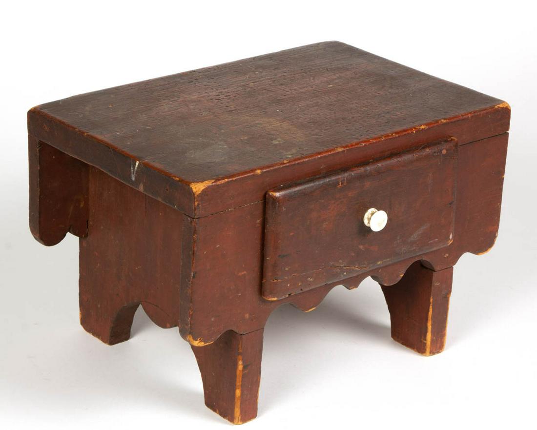 AMERICAN COUNTRY PAINTED PINE FOOT STOOL: AMERICAN COUNTRY PAINTED PINE FOOT STOOL, having one-drawer with likely original porcelain knob, with cut-out skirt and feet. Retains likely original red-painted surface. Mid 19th century. 8 1/4" H, 1