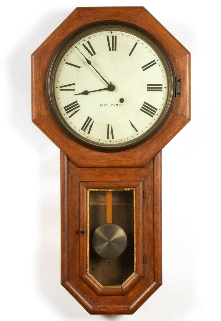 SETH THOMAS OAK SCHOOLHOUSE WALL CLOCK: SETH THOMAS OAK SCHOOLHOUSE WALL CLOCK, octagonal top, above a hinged door, dial with painted tin face with Roman Numerals and marked "SETH THOMAS", original paper label to interior "Manufactured By /