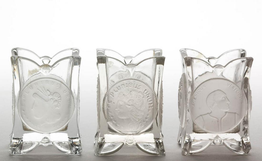 U. S. COIN / SILVER AGE (OMN) TOOTHPICK HOLDERS, LOT OF: U. S. COIN / SILVER AGE (OMN) TOOTHPICK HOLDERS, LOT OF TWO, colorless with frosted coins, featuring one dollar coins. Together with a Columbian Coin toothpick holder. Three pieces total. Central Glas