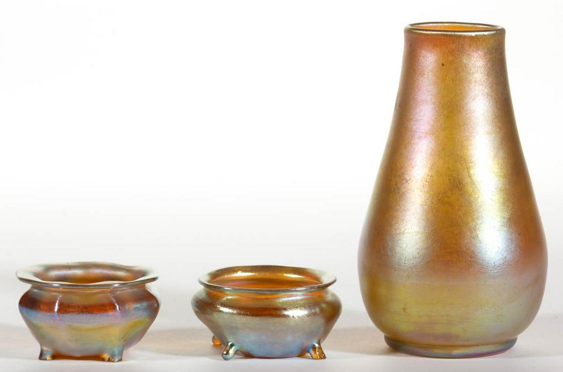 TIFFANY GOLDEN IRIDESCENT ART GLASS ARTICLES, LOT OF: TIFFANY GOLDEN IRIDESCENT ART GLASS ARTICLES, LOT OF THREE, comprising a small baluster-form vase and two footed salt dishes, each signed. Tiffany Studios. Early 20th century. Vase: 5" H. Salts: 2 1/4