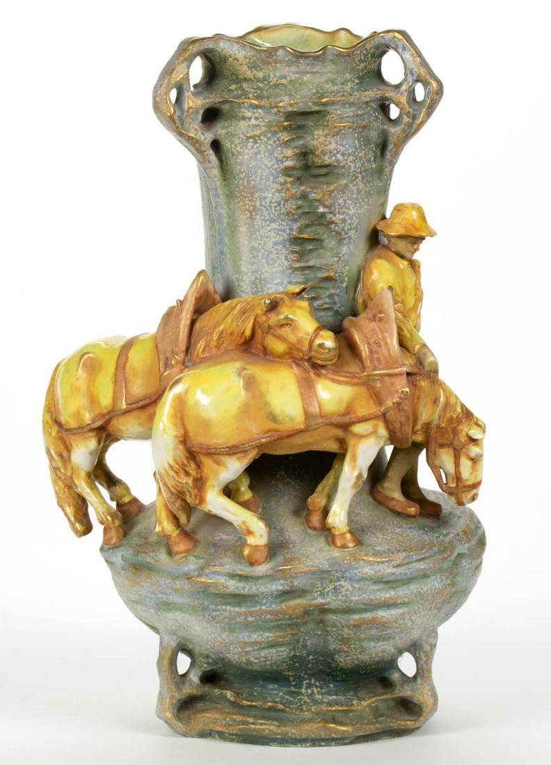 AMPHORA FIGURAL CERAMIC VASE: AMPHORA FIGURAL CERAMIC VASE, featuring a farmer leading two draft horses, with sunset color palate, around a blue- and green-glazed craggy bodied base with three open handles at top, having gilt acce