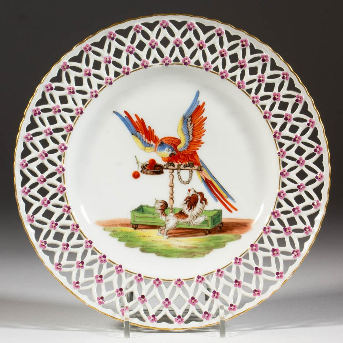 GERMAN MEISSEN PORCELAIN RETICULATED PLATE: GERMAN MEISSEN PORCELAIN RETICULATED PLATE, having a polychrome hand-painted scene featuring a King Charles Spaniel barking at an agitated, chained parrot with delicate violets evenly spaced on border