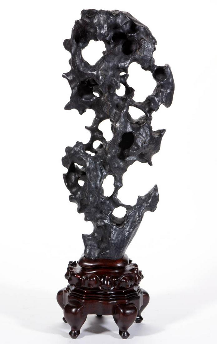 CHINESE SCHOLAR’S STONE WITH STAND: CHINESE SCHOLAR’S STONE WITH STAND, cloud-form black stone with quartz inclusions, fitted on a likely rosewood five-footed stand. Qing dynasty (1644 to 1912), or later. 20 1/4" H x 8 1/2" W stone, 2