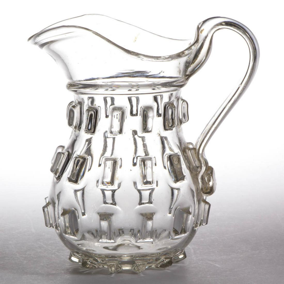 CLEAT QUART PITCHER: CLEAT QUART PITCHER, colorless lead glass, baluster-form body with a molded neck ring, tooled spout, applied solid strap handle, and polished pontil mark. Probably New England. 1850-1870. 8 1/4" H, 4 