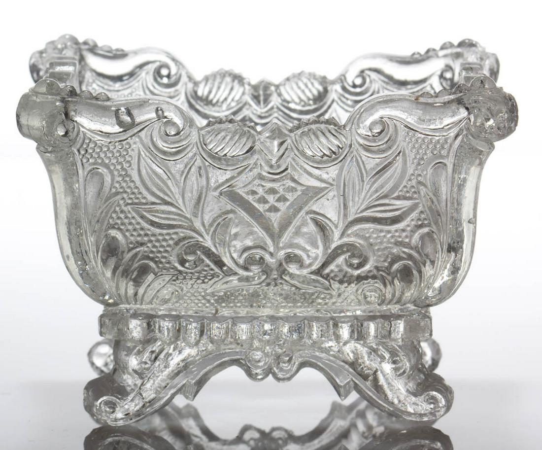 PE-1 PROVIDENCE MARKED PRESSED OPEN SALT: PE-1 PROVIDENCE MARKED PRESSED OPEN SALT, colorless, eagle-headed shield on each end, "PROVIDENCE" in base, raised on four scrolled feet. Very rare. Providence Flint Glass Co. 1835-1850. 2 1/4" H, 2 1