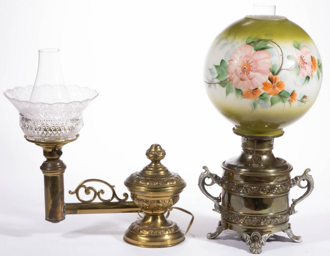 ASSORTED EMBOSSED METAL KEROSENE LAMPS, LOT OF TWO: ASSORTED EMBOSSED METAL KEROSENE LAMPS, LOT OF TWO, comprising a single-arm desk/piano lamp having a weighted base and colorless pressed glass gas shade with etched decoration, and a cylindrical bucke