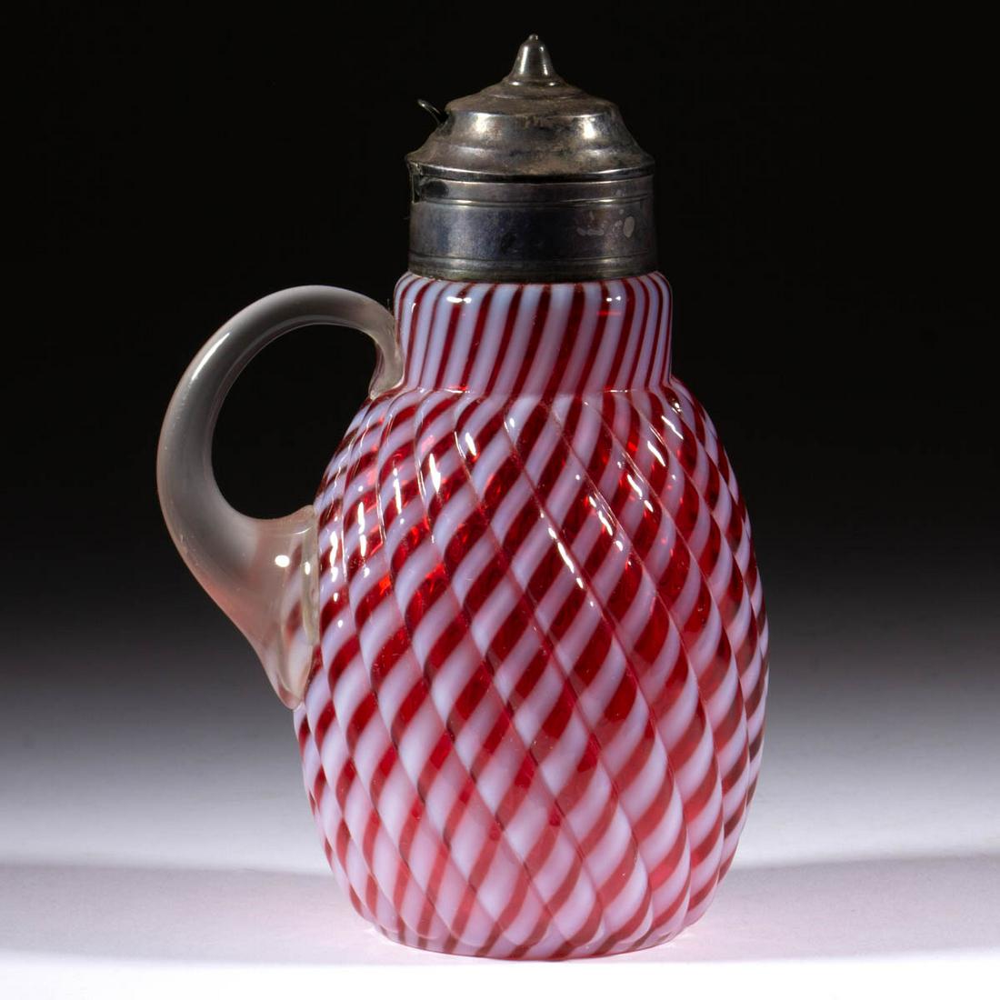 REVERSE SWIRL SYRUP PITCHER: REVERSE SWIRL SYRUP PITCHER, cranberry opalescent, with applied colorless/clamwater handle, period lid. Buckeye Glass Co. or Model Flint Co. 1888-1902. 6 3/4" HOA. Undamaged. Literature: Parallels Hea